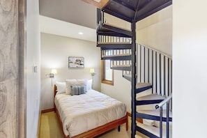 A bedroom with a bed, a wall-mounted lamp, a painting, and a spiral staircase. - Cozy condo with fireplace, W/D, wifi & ski in / out access (Mountain Village)