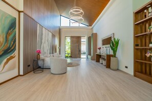 A spacious hallway with a high ceiling, a modern light fixture, a sofa, and a wooden bookshelf. - Ruby Luxury Villa, 4 Bed Private Pool Paradise (Rawai)