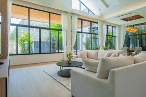 A spacious living room with large windows, a sofa, a coffee table, and a hanging light fixture. - Ruby Luxury Villa, 4 Bed Private Pool Paradise (Rawai)