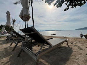 Ein Strand mit Liegestühlen und Sonnenschirmen, einem wolkenlosen Himmel und ruhigem Meer.