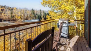 A balcony with a grill, a chair, and a view of a forest with autumn foliage. - Fantastic, ski-in/out condo with patio, fireplace, grill & Washer/Dryer (Mountain Village)