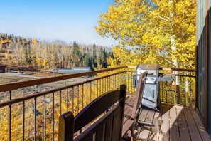 A balcony with a grill, a chair, and a view of a forest with autumn foliage. - Fantastic, ski-in/out condo with patio, fireplace, grill & Washer/Dryer (Mountain Village)