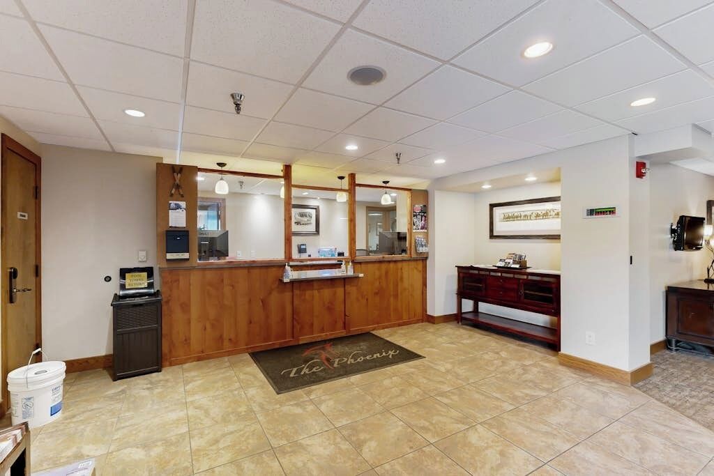 A reception area with a wooden counter, a reception desk, a small trash bin, a coffee machine, and a framed picture on the wall.