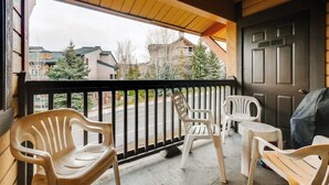 Een overdekt terras met plastic stoelen en een tafel, een donkere deur, en uitzicht op huizen en bomen.