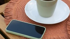 A smartphone on a woven placemat, a cup of tea on a saucer, and a bed with white bedding. - Checha Ático (Candelaria)