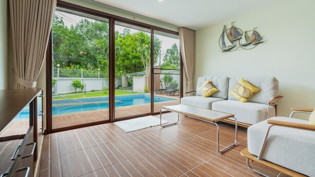 A spacious living area with a large sliding glass door leading to a pool, a sofa with cushions, and a small table. - NEW Tulip 4 Bedroom Pool Villa  Chalong Phuket (Chalong)