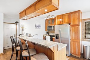 A kitchen with wooden cabinets, a granite countertop, stainless steel appliances, and a bar area with stools. - Classic ski condo with hot tub, pool, high-speed WiFi & fireplace (Steamboat Springs)