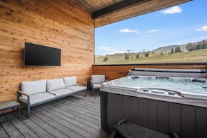 Eine Holzterrasse mit Whirlpool, einer Sitzecke und einem an der Wand montierten Fernseher.