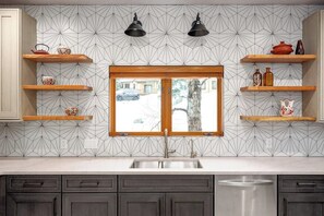 Eine Küche mit backsplash in geometrischem Muster, Holzregalen, einem Fenster und einer Spüle aus Edelstahl.
