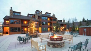 A multi-story building with outdoor seating, a fire pit, and a well-lit patio area. - Kutuk 101 - First-Floor Condo with Shared Hot Tub, WiFi, Gas Fireplace, and Full Kitchen (Steamboat Springs)