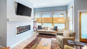 A living room with a sofa, a coffee table, a fireplace, and a television mounted on the wall. - Kutuk 101 - First-Floor Condo with Shared Hot Tub, WiFi, Gas Fireplace, and Full Kitchen (Steamboat Springs)