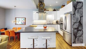 A modern kitchen with a central island, bar stools, a refrigerator, and a dining area with chairs. - Kutuk 101 - First-Floor Condo with Shared Hot Tub, WiFi, Gas Fireplace, and Full Kitchen (Steamboat Springs)
