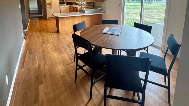 Eine moderne Küche mit Holzschnitzschränken, einem Esstisch mit Stühlen und einem großen Fenster mit Blick ins Freie.
