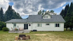 Ein zweistöckiges Haus mit einer Veranda, einer kleinen Terrasse und einem Feuerkorb im Garten.