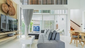 A modern living room with a grey sofa, a flat-screen TV, and a dining area with wooden chairs. - NEW Lavender Private Pool Villa, Rawai , Phuket (Nai harn, Rawai)