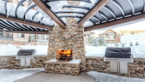 Ein Steinkamin mit Feuer, umgeben von einer Steinwand und Metallbalken, mit Schnee auf dem Boden.