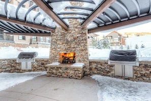 Ein Steinkamin mit Feuer, umgeben von einer Steinwand und Metallbalken, mit Schnee auf dem Boden.
