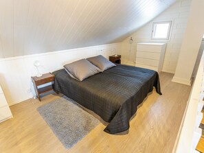 A bedroom with a bed, bedside table, lamp, dresser, and a window.