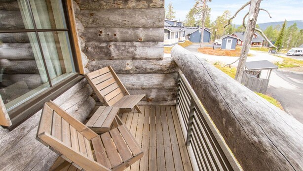 Un ponte di legno con panchina e tavolo, l'esterno di una baita di tronchi e vista su una zona residenziale con case.
