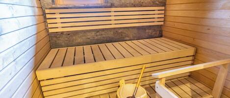 Un sauna con bancos de madera, un ventanal pequeño y un cubo con un cepillo.