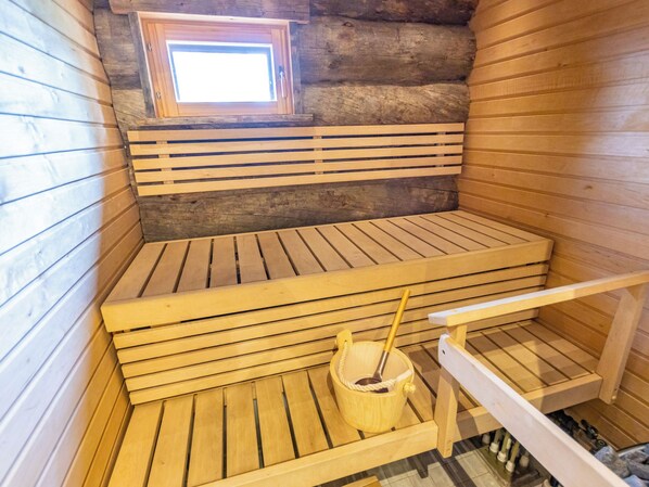 Un sauna con bancos de madera, un ventanal pequeño y un cubo con un cepillo.
