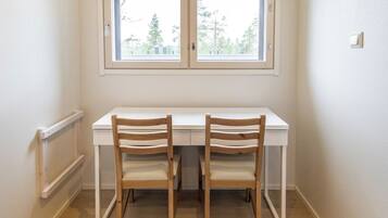 A corner room with a white desk and two wooden chairs, a window with a view of trees, and a white wall.