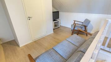 A room with a sofa, a chair, a television on a stand, and a door.