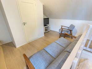 Una habitación con sofá, una silla, televisor sobre un mueble y una puerta.