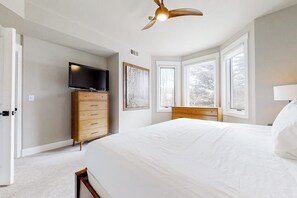 A bedroom with a bed, a TV on a dresser, a ceiling fan, and large windows. - Ski view condo walkable to the lifts with pools, hot tubs, WiFi, and fireplace (Steamboat Springs)