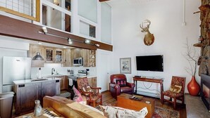 A spacious living area with a kitchen, a fireplace, and a mounted deer head. - Two-Story Ski-In Condo w/Free WiFi, Gas Fireplace, Private W/D, Shared Hot Tub (Steamboat Springs)