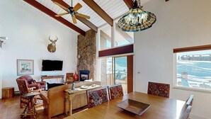 A spacious living area with a wooden dining table, a fireplace, a mounted deer head, and a large window with a view. - Two-Story Ski-In Condo w/Free WiFi, Gas Fireplace, Private W/D, Shared Hot Tub (Steamboat Springs)