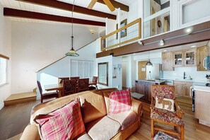 Ein geräumiger Wohnbereich mit hohen Decken, einem Esstisch mit Stühlen, einer Küche mit Holzschränken und einer Treppe zu einer oberen Ebene.