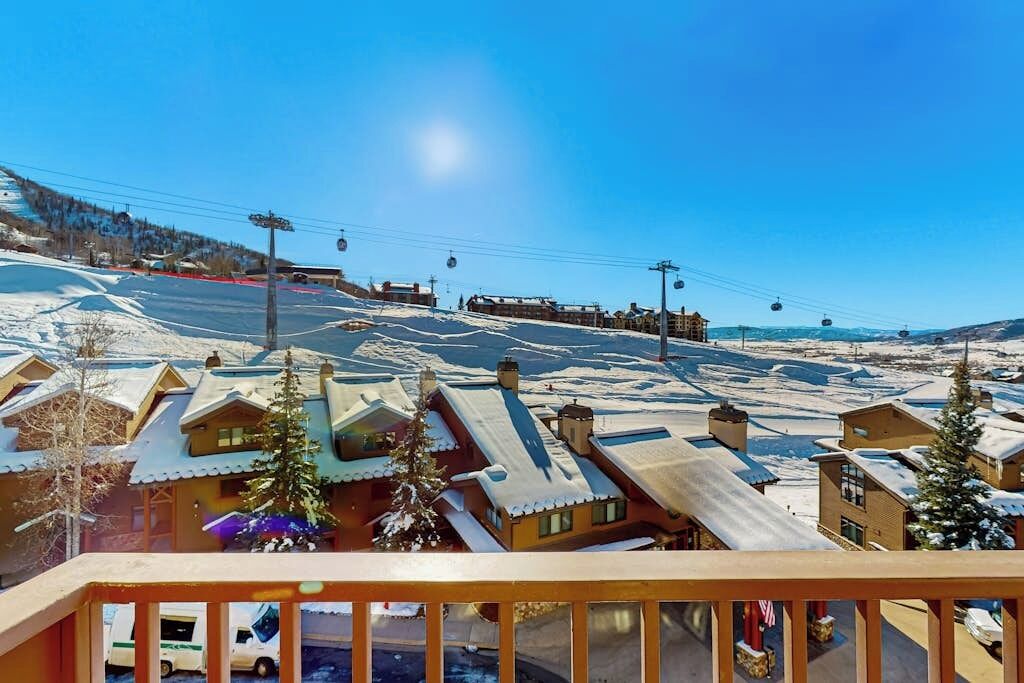 Une station de ski aux toits enneigés, avec un télésiège et un ciel bleu dégagé.