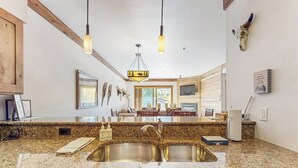 A kitchen with granite countertops, a double sink, pendant lighting, and a dining area visible through the window. - Updated, Second-Floor Condo with WiFi, Mountain Views, Outdoor Pool, & Hot Tub (Steamboat Springs)