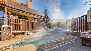 A hot spring area with a wooden fence, benches, and a building in the background. - Updated, Second-Floor Condo with WiFi, Mountain Views, Outdoor Pool, & Hot Tub (Steamboat Springs)
