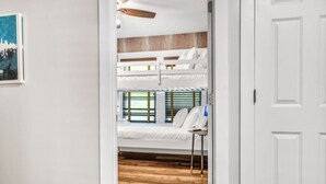 Une pièce avec un lit superposé, une petite table avec une chaise et une porte donnant sur une autre pièce.