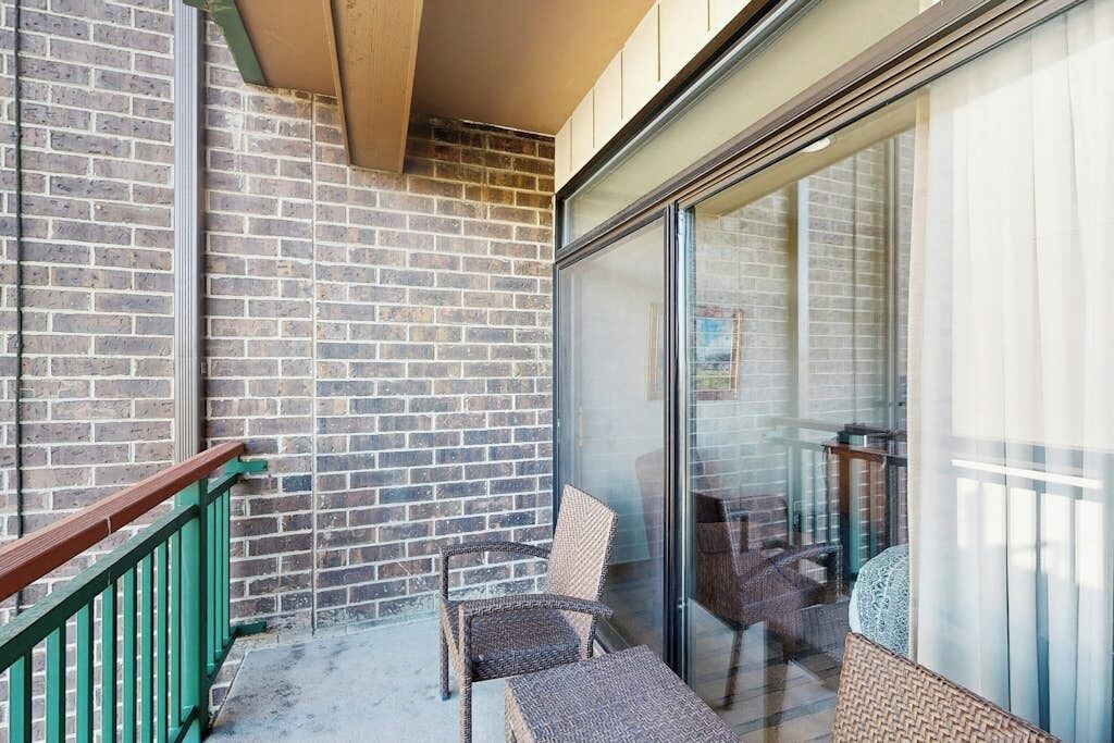 Un balcone con un muro in mattoni, una porta in vetro, mobili in vimini e una ringhiera verde.