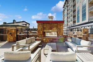 A rooftop patio with outdoor seating, a stone fireplace, and a view of a high-rise building. - Ski-in/ski-out condo in Sheraton with pool, hot tub, mountain view & fireplace (Steamboat Springs)
