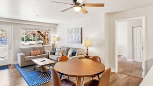 Ein Wohnzimmer mit einem runden Holztisch, zwei Sofas, einem Deckenventilator und einem großen Fenster.