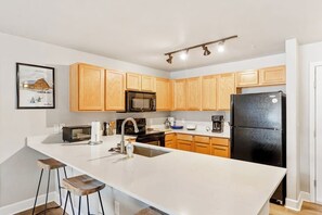 A kitchen with wooden cabinets, a black refrigerator, a microwave, a sink, and a bar stool. - Renovated, ground-floor condo with pool, hot tubs & gym - steps to gondola (Steamboat Springs)