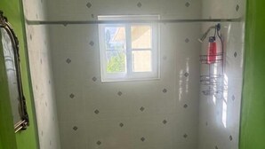 A bathroom with a shower, toilet, and sink, featuring patterned tiles and a small window.