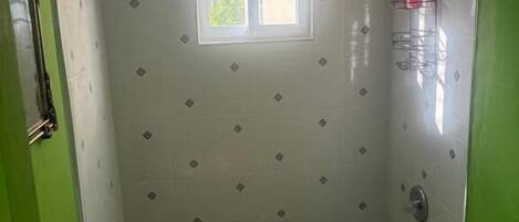 A bathroom with a shower, toilet, and sink, featuring patterned tiles and a small window.