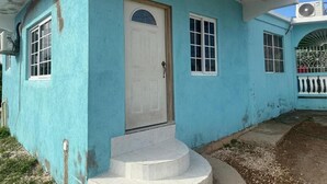 A single-story building with a white door, two windows, and a small porch.