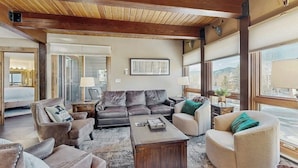Ein geräumiges Wohnzimmer mit Holzboden, Ledersofas, einem Couchtisch und großen Fenstern mit Blick.