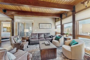 Ein geräumiges Wohnzimmer mit Holzboden, Ledersofas, einem Couchtisch und großen Fenstern mit Blick.