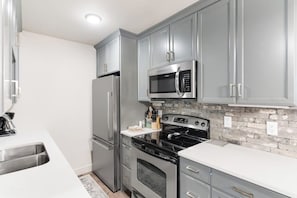 A modern kitchen with stainless steel appliances, grey cabinetry, and a brick backsplash. - Ski-In/Ski-Out Condo with Shared Hot Tubs, Saunas, Patio, Shuttle to Ski Resort (Steamboat Springs)