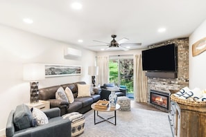 A living room with a sofa, coffee table, fireplace, television, and a ceiling fan. - Ski-In/Ski-Out Condo with Shared Hot Tubs, Saunas, Patio, Shuttle to Ski Resort (Steamboat Springs)