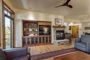 A living room with a fireplace, television, and built-in shelving. - Stylish condo near slopes with fireplace, balcony, grill, pools, & hot tubs (Steamboat Springs)