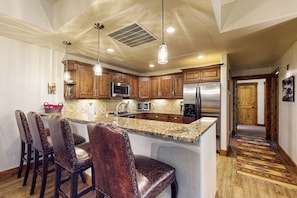A kitchen with wooden cabinets, stainless steel appliances, and a central island with bar stools. - Stylish condo near slopes with fireplace, balcony, grill, pools, & hot tubs (Steamboat Springs)