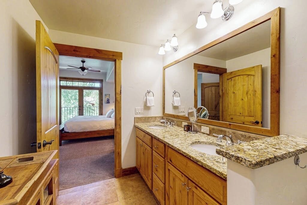 A bathroom with a double sink, wooden cabinets, a large mirror, and a ceiling fan.